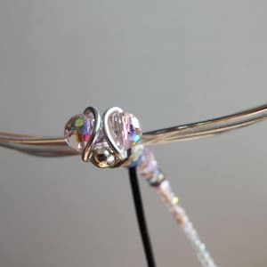 Könnte beinhalten: Nahaufnahme eines handgefertigten Libellenornaments. Die Libelle hat irisierende Kristallperlen für die Augen und einen Perlenkörper. Die Flügel sind aus silberfarbenem Draht gefertigt. Die Libelle ist ein dekoratives Objekt.