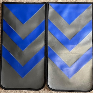 May include: Two rectangular, padded automotive seat protectors. Each has a gray background with blue chevron stripes and a black border. The protectors are designed to shield car seats from wear and tear.
