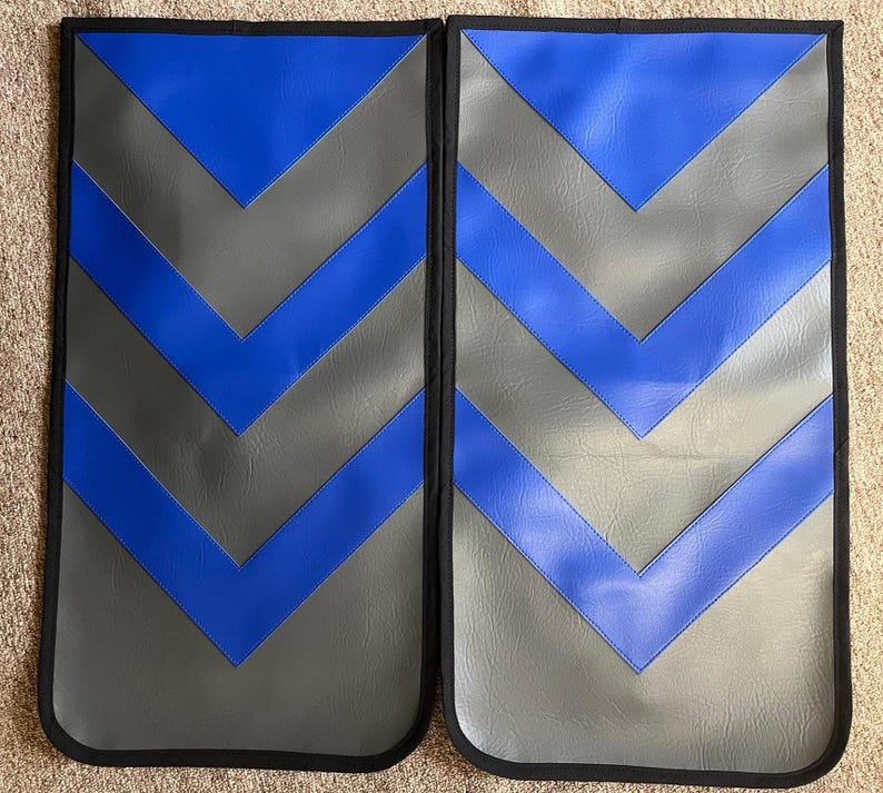 May include: Two rectangular, padded automotive seat protectors. Each has a gray background with blue chevron stripes and a black border. The protectors are designed to shield car seats from wear and tear.