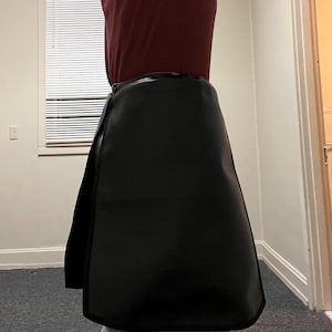 May include: Black wrap skirt made of a smooth material. The skirt has a simple design with a wrap-around style and a slight A-line shape. The skirt is shown from the waist down.