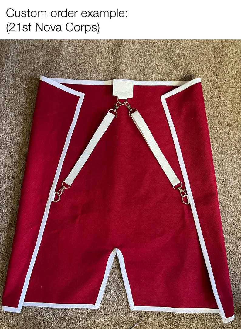 May include: Red fabric garment with white trim and straps, featuring metal hardware. The garment has a split at the bottom and the text "Custom order example: (21st Nova Corps)" at the top.