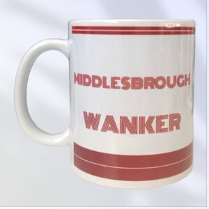 May include: White ceramic mug with a curved handle. The mug features the words "Middlesbrough Wanker" in red, with red stripes at the top and bottom. The mug is designed for hot beverages.