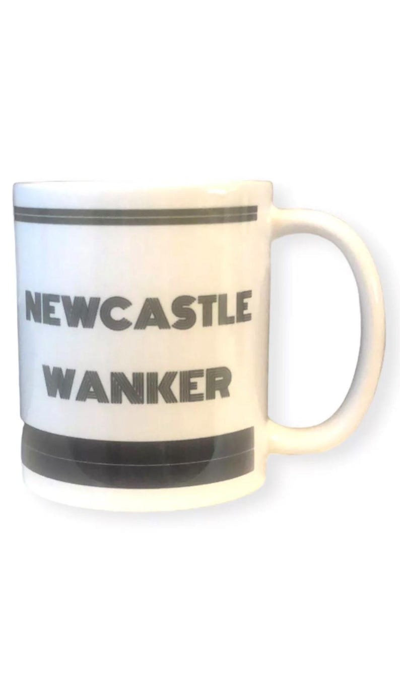 May include: White ceramic mug with a black handle and rim. The mug features the words "NEWCASTLE WANKER" in bold, black capital letters. The mug has a simple, clean design.