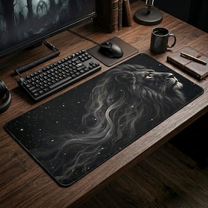 May include: Black mousepad featuring a detailed illustration of a lion's head with a flowing mane, set against a starry night sky. The design is predominantly black and gray, with subtle highlights. The mousepad is rectangular and sits on a wooden desk.