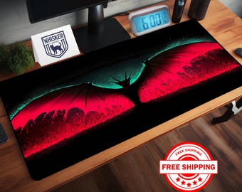May include: A black gaming mouse pad with a red and green dragon silhouette design. The dragon's wings are spread wide and the background is a dark, textured surface.