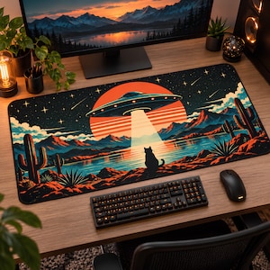 May include: A rectangular desk mat featuring a vibrant illustration of a flying saucer hovering over a desert landscape at sunset. The scene includes a silhouette of a cat, cacti, mountains, a lake, and a large orange sun against a starry night sky.