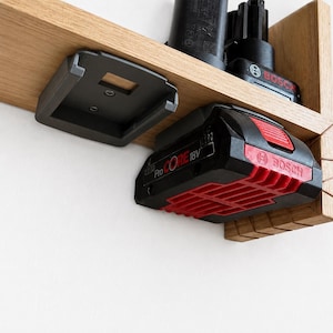 Könnte beinhalten: Ein schwarzer und roter Bosch ProCORE 18V Akku ist an einem Holzregal befestigt. Der Akku hat ein rotes Gittermuster auf der Unterseite und das Bosch-Logo. Ein schwarzer Akkuhalter ist oben am Regal montiert.