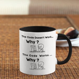 Può includere: Tazza in ceramica bianca con interno e manico neri. La tazza presenta il testo "The Code Doesn't Work... Why?" e "The Code Works... Why?" con un'immagine a cartoni animati di una persona al computer.