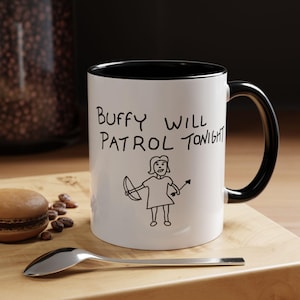 Może przedstawiać: Biały ceramiczny kubek z czarnym wnętrzem i uchwytem. Kubek zawiera napis "Buffy Will Patrol Tonight" oraz ręcznie rysowaną ilustrację postaci z łukiem i strzałą. Widoczna jest również łyżka i makaronik.