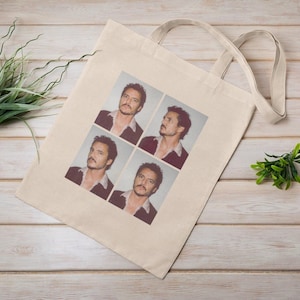 Peut inclure: Un sac fourre-tout en toile beige avec quatre images d'un homme en veste sombre et chemise ouverte. Les images sont disposées en carré, montrant le visage de l'homme dans différentes poses. Le sac a deux anses.