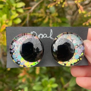 May include: A pair of black and iridescent glitter round earrings. The earrings are on a black card with the word "Opal" written on it.