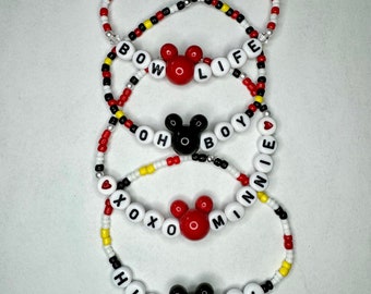 May include: Four beaded bracelets with Mickey Mouse ears charms. The bracelets spell out "BOW LIFE", "OH BOY", "XOXO MINNIE", and "HIYA PAL".
