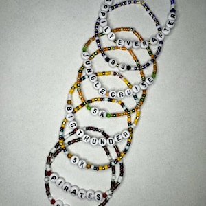May include: A set of eight colorful beaded bracelets with different words and phrases, including "Happily Ever After", "Jungle Cruise", "Big Thunder", and "Pirates".