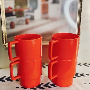 Puede incluir: Cuatro tazas de plástico de color naranja brillante apiladas en dos juegos de dos. Las tazas tienen un diseño sencillo y son perfectas para el uso diario.