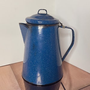 Puede incluir: Una cafetera de esmalte azul con un acabado moteado y una tapa. La cafetera tiene un asa y un pico.