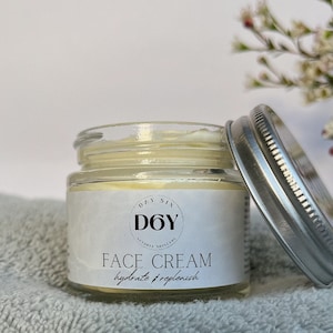 May include: A glass jar of face cream with a silver lid. The jar is labeled "Day Six D6Y Natural Skincare Face Cream hydrate + replenish".