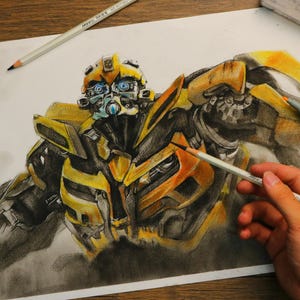 Pode incluir: Um desenho detalhado a lápis e marcador do personagem Bumblebee de Transformers em amarelo e preto. A obra de arte está em papel branco, com lápis, marcadores e uma borracha em volta do desenho. Uma mão segura um lápis.