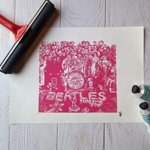 May include: A pink and white linocut print of the Beatles album cover "Sgt. Pepper's Lonely Hearts Club Band". The print features a crowd of people surrounding the Beatles, with the band's name and album title in large white letters.