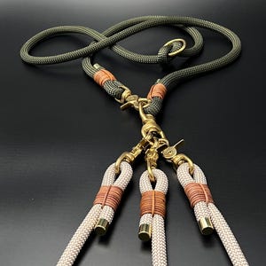 Op de afbeelding: Een groene en beige touwhalster met drie afzonderlijke halsters die aan een messing gesp zijn bevestigd. De halsters zijn gemaakt van beige touw met bruine accenten.