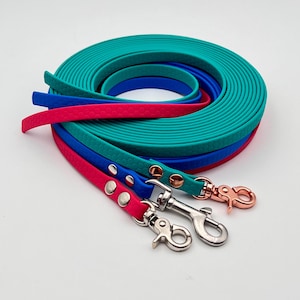 Pode incluir: Três trelas para cão longas e planas enroladas juntas em turquesa brilhante, azul real e rosa choque. Cada trela apresenta um padrão de favo de mel texturizado, rebites de metal prateado ou ouro rosa e ganchos giratórios a condizer.