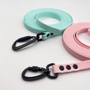 Könnte beinhalten: Zwei lange, aufgerollte Leinen in Pastell-Minzgrün und zartem Rosa. Jede Leine verfügt über ein strukturiertes Wabenmuster, einen schwarzen Metallkarabiner mit Schraubverschluss und drei schwarze Nieten zur Befestigung am Gurtband.