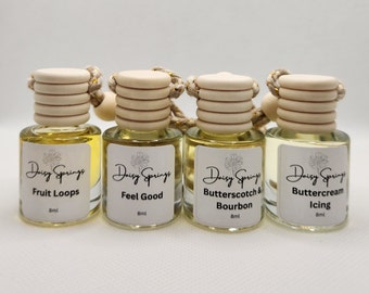May include: Four small glass bottles with wooden stoppers and string hangers. Each bottle contains a yellow liquid and has a white label with black text. The labels read "Daisy Springs Fruit Loops 8ml", "Daisy Springs Feel Good 8ml", "Daisy Springs Butterscotch & Bourbon 8ml", and "Daisy Springs Buttercream Icing 8ml".