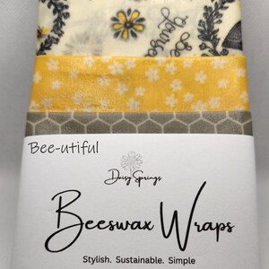 May include: A stack of beeswax wraps with various patterns, including floral and bee designs. The wraps are labeled "Bee-utiful" and "Beeswax Wraps" with size details: Small - 6" x 9", Medium - 10" x 10", and Large - 11" x 14".