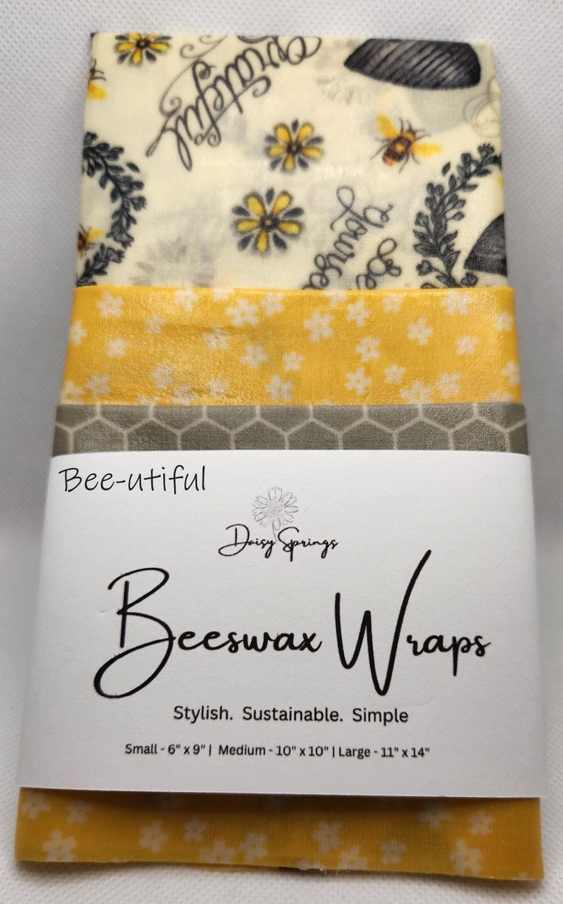 May include: A stack of beeswax wraps with various patterns, including floral and bee designs. The wraps are labeled "Bee-utiful" and "Beeswax Wraps" with size details: Small - 6" x 9", Medium - 10" x 10", and Large - 11" x 14".