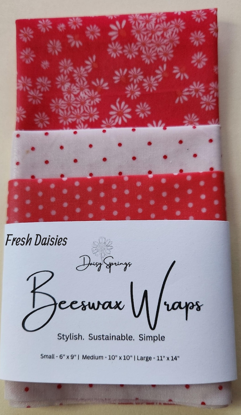 May include: A stack of red and white beeswax wraps with floral and polka dot patterns. The label reads "Fresh Daisies" and "Beeswax Wraps". Sizes are small (6" x 9"), medium (10" x 10"), and large (11" x 14").