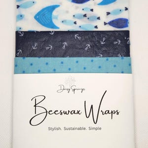 May include: A set of beeswax wraps with various nautical and aquatic patterns. Designs include fish, anchors, and polka dots in shades of blue and white. The wraps are labeled "Daisy Springs Beeswax Wraps". The words "Lake Life" are in the top left corner.