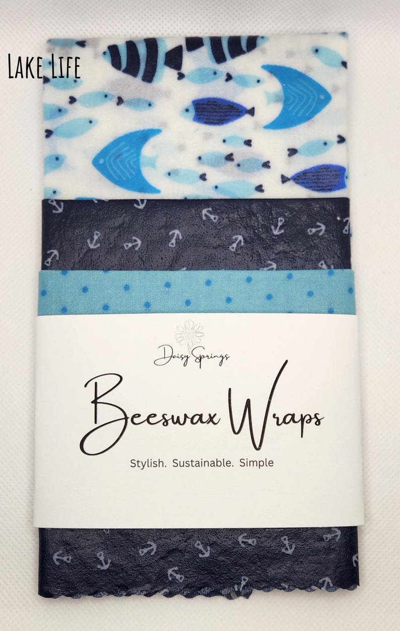 May include: A set of beeswax wraps with various nautical and aquatic patterns. Designs include fish, anchors, and polka dots in shades of blue and white. The wraps are labeled "Daisy Springs Beeswax Wraps". The words "Lake Life" are in the top left corner.