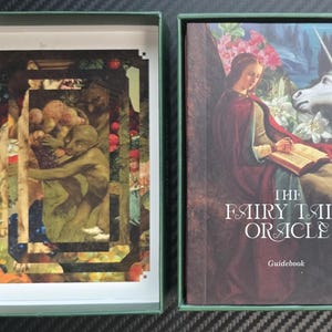 May include: An open green box with a deck of cards and a guidebook. The deck of cards features a collage of figures and foliage. The guidebook cover displays a woman, a unicorn, and the text "THE FAIRY TALE ORACLE".