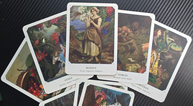 May include: A collection of tarot cards featuring illustrations of figures and scenes. The central card displays a woman labeled "Maiden." Other cards include "Goblin," "Steed," and "Sorcerer." The cards have white borders and are arranged on a dark surface.