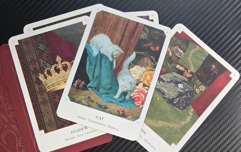 May include: A collection of tarot cards featuring illustrations of a golden crown, white cats, and floral arrangements. The cards have white borders and are stacked on a red book. The card with the cats is labeled "CAT".