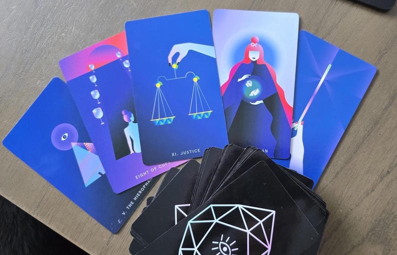 May include: A deck of tarot cards with vibrant illustrations. Several cards are fanned out, displaying images of scales, a figure with a globe, and other symbolic designs. The cards have a dark background with geometric patterns.