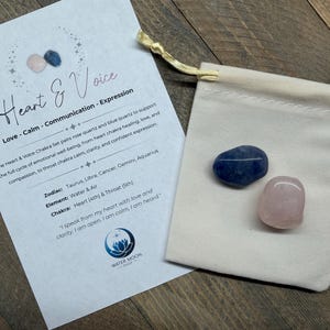 May include: A set of Heart & Voice chakra stones, including a blue quartz and a rose quartz, presented in a small beige drawstring bag. A card with text about the set is next to the bag. The text includes the words "Heart & Voice".
