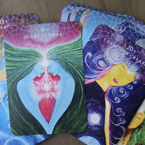 May include: A set of colorful oracle cards with images of people and nature. The cards feature numbers and text, including "Heart Flower", "Conscious Creator", and "Star Consciousness".