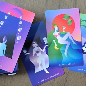 May include: A deck of tarot cards with colorful illustrations. The cards feature images of figures, cups, and palm trees. The Eight of Cups, The Empress, The High Priestess, and Four of Cups are visible. The cards have a gradient color scheme of purple, blue, and pink.