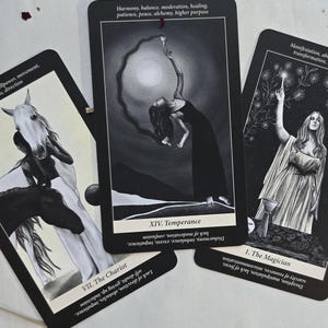 May include: Three tarot cards with black backgrounds and white illustrations are displayed. The cards feature images of a horse, a woman, and a figure in a flowing gown. Text on the cards includes "The Chariot," "Temperance," and "The Magician."