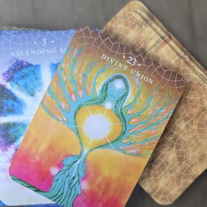 May include: Two tarot cards, one with a blue and purple background and the text "Ascending Soul" and the other with a yellow, orange, and green background and the text "Divine Union" with a number 23.