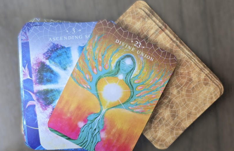 May include: Two tarot cards, one with a blue and purple background and the text "Ascending Soul" and the other with a yellow, orange, and green background and the text "Divine Union" with a number 23.