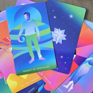 May include: A collection of colorful tarot cards with vibrant illustrations. The Knight of Pentacles card features a figure in green and blue. Other cards display celestial and geometric designs, with text including "The Chariot" and "Lovers".