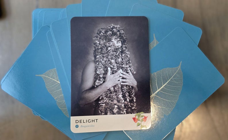May include: A black and white tarot card with a person wearing a leafy headpiece and holding their hands to their chest. The card is titled "DELIGHT" with the text "#MagnificentYou" below the title.
