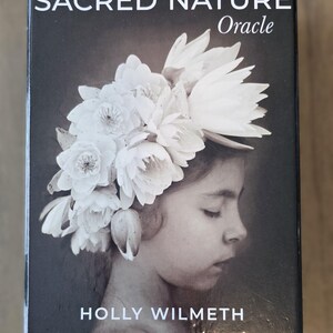 May include: A black box with the text "SACRED NATURE Oracle" and "HOLLY WILMETH" on the front. The box features a black and white photograph of a young girl with a crown of white flowers on her head.