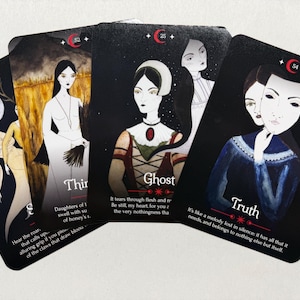 May include: Four rectangular oracle cards with black borders and red crescent moon symbols. The cards feature illustrations of figures in various attire, including a mask, and text labels such as Ghost and Truth, with descriptive paragraphs below.