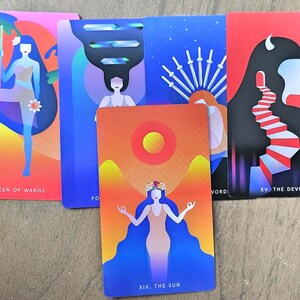 May include: A collection of tarot cards featuring vibrant illustrations. The cards display figures and symbols in shades of pink, blue, orange, and red. The cards include the Queen of Wands, The Sun, and The Devil, with text labels.