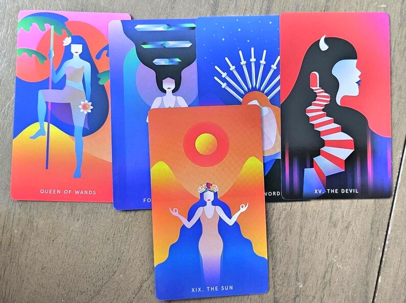 May include: A collection of tarot cards featuring vibrant illustrations. The cards display figures and symbols in shades of pink, blue, orange, and red. The cards include the Queen of Wands, The Sun, and The Devil, with text labels.