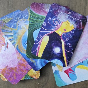 May include: A set of colorful oracle cards with various images and text. The cards feature a variety of themes, including "Star Consciousness", "Heart", "Conscious Creator", "Rise Above", "Top Doing, Start Being", and "Investment".