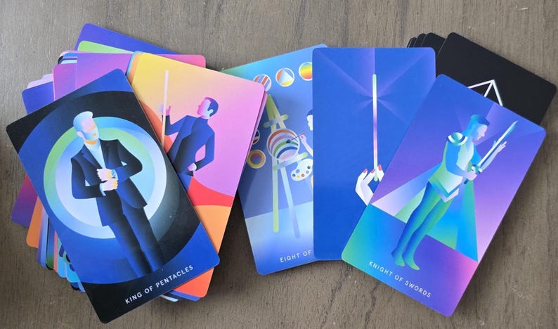 May include: A deck of tarot cards with colorful geometric illustrations. The cards feature figures and symbols, including the "King of Pentacles" and "Knight of Swords." The color palette includes blues, purples, and yellows. The cards are arranged on a wooden surface.