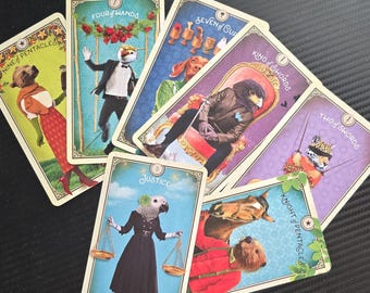 Peut inclure: Plusieurs cartes de tarot avec des illustrations d'animaux. Les cartes affichent des titres tels que "Nine of Pentacles", "Four of Wands" et "Justice". L'œuvre d'art comprend un ours, un perroquet et un cheval.